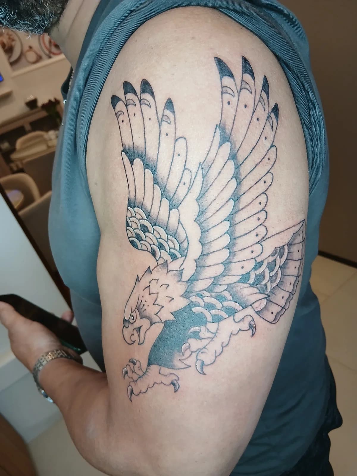 Tatuagem de ave com asas abertas no ombro.